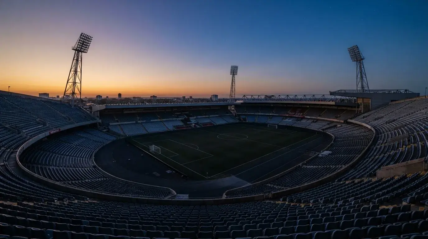 Een leeg voetbalstadion met lichtmasten bij schemering