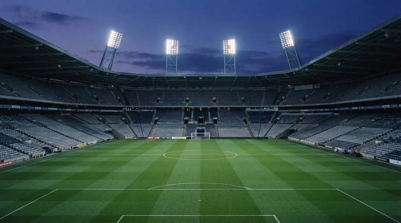 Een leeg voetbalstadion met lichtmasten bij schemering
